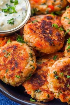 some crab cakes are on a black plate with a small bowl of ranch dressing next to it