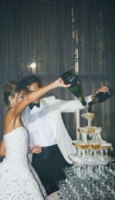 a bride and groom are standing in front of a wedding cake with champagne being poured on it