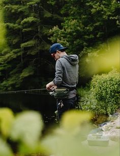 a man standing on the edge of a body of water while holding onto a fishing rod