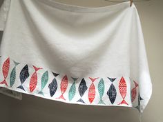 a white towel hanging from a clothes line with fish on it's side and red, green, and blue designs