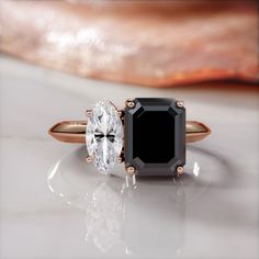 two engagement rings with an oval black diamond and a round white diamond on each side