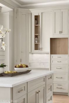 a bowl of fruit is sitting on the counter in this white kitchen with wood flooring