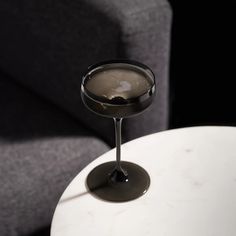 a martini glass sitting on top of a white table next to a gray couch in a living room