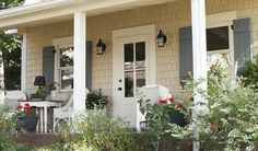 a white house with blue shutters and red flowers on the front porch, along with potted plants