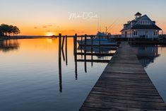 the sun is setting over some water and boats are docked in front of a house