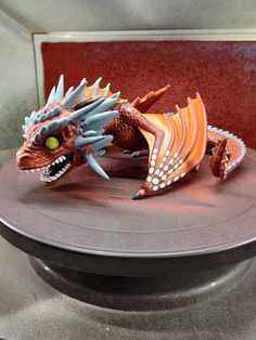 an orange and blue dragon figurine sitting on top of a round metal plate