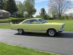 an old yellow car is parked on the side of the road in front of a house