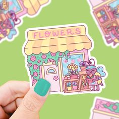 a person holding up a sticker that says flowers in front of a flower shop