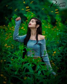 a woman standing in the grass with her arms up and eyes closed, looking upward