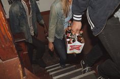 two people are walking down the stairs with beer bottles in their hands and one person is holding a bag