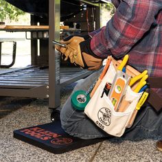 a man sitting on the ground with tools in his hand and an open tool bag next to him