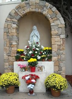 flowers are placed in front of a stone arch with a statue behind it and potted plants on either side