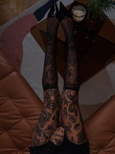 a tattooed woman laying on top of a brown couch