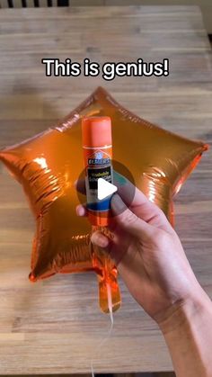 someone is holding an orange spray bottle in front of a star shaped balloon that says, this is genius