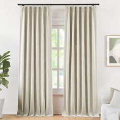 a living room with a white couch and window covered in beige curtain panels, next to a potted plant