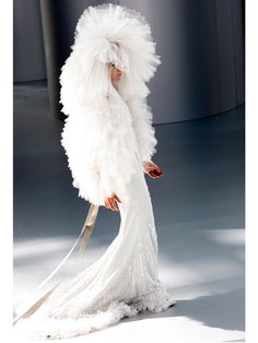 a woman in a white feathered dress holding a large pair of scissors on the runway