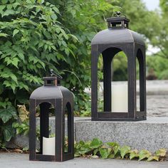 two black lanterns sitting next to each other in front of some bushes and trees with green leaves