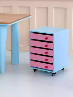 a pink and blue dresser next to a wooden table with three drawers on each drawer