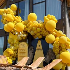 a bunch of yellow balloons hanging from the side of a building with lounge chairs in front of it