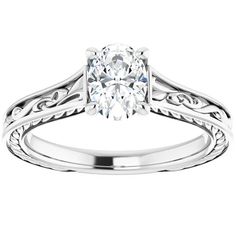 a white gold engagement ring with an oval cut diamond in the center and filigrees around the band