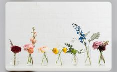 several vases with flowers in them sitting on a table next to a brick wall