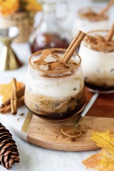 two glasses filled with ice cream and cinnamon on top of a cutting board next to an apple