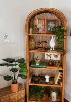 a wicker shelf with plants and books on it in the corner of a room