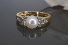 RING SIZE: 7 (Sizable by your local jeweler) DETAILS: Metal: 10k Yellow Gold Gemstone: 1x 6.5mm White Pearl, 6 round brilliant cut diamonds (Approx. 1.7mm in diameter each/ Approx. 0.12ctw) 8 Tapered Baguette cut diamonds ( Approx. 2.5mmx1mm/ Approx 0.24 ctw) Weight: 2.4 grams MEASUREMENTS: - 6.5 mm from north to south - 2.0mm shank - sits 7.1mm above finger Round Cut Diamond Pearl Ring For Anniversary, Classic Pearl Ring With Diamond Accents For Anniversary, Anniversary Pearl Ring With Vvs Clarity Diamond, Classic Diamond Pearl Ring For Anniversary, Classic Yellow Gold Pearl Ring With Cubic Zirconia, Anniversary Pearl Ring With Single Cut Diamonds, Classic Pearl Ring With Diamonds For Anniversary, Classic Pearl Ring With Single Cut Diamonds For Gift, Classic Pearl Ring With Single Cut Diamonds As Gift