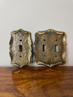 two decorative metal switch plates sitting on top of a wooden table next to a white wall