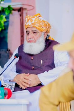 a man with a long white beard wearing a yellow turban sitting in front of a microphone