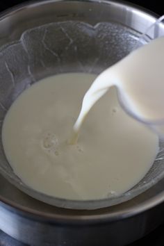 milk being poured into a metal bowl on top of a stove burner with a spoon in it