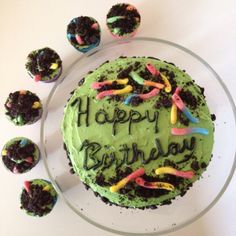 a birthday cake with green frosting and sprinkles on it, surrounded by cupcakes