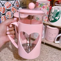 a person is holding a pink coffee mug in front of some cups and other items