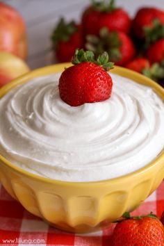 a yellow bowl filled with whipped cream and two strawberries next to it on a checkered table cloth