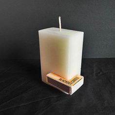 a white candle sitting on top of a black table next to a matchbox with matches