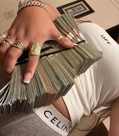 a woman is holding stacks of money in her hand and wearing gold rings on her fingers