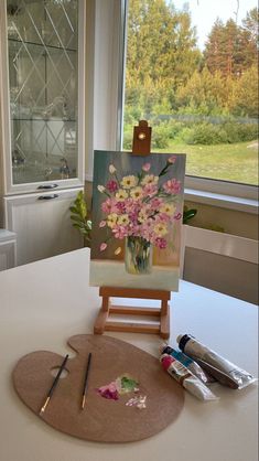 an easel with flowers on it sitting next to a painting and paintbrushes