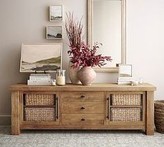 a vase with flowers on top of a wooden table next to a mirror and wicker baskets