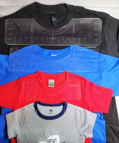 four different colored shirts are next to each other on a white wooden surface with rulers