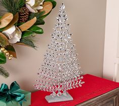 a silver christmas tree sitting on top of a red blanket next to a bouquet of flowers