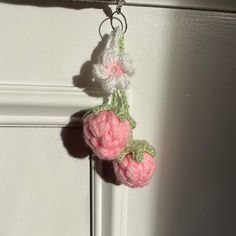 two crocheted strawberries hanging from a hook on a door handle in front of a white wall