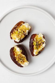 three stuffed dates on a white plate topped with whipped cream and pistachio sauce