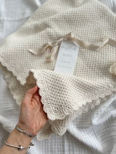 a woman's hand holding onto a white knitted blanket on top of a bed