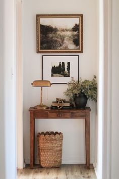 a wooden table with a basket on top of it next to a painting and lamp