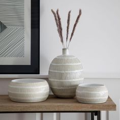 three white vases sitting on top of a wooden table next to a framed photograph