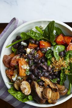 a white bowl filled with black beans, mushrooms and spinach on top of a wooden table