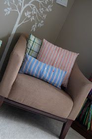 a chair with several pillows on it and a tree painted on the wall behind it