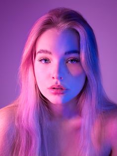 a woman with long blonde hair and blue eyes is looking at the camera while she has pink light on her face