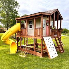 a wooden play house with a slide in the grass