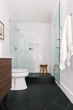 a white toilet sitting in a bathroom next to a walk in shower and wooden stool